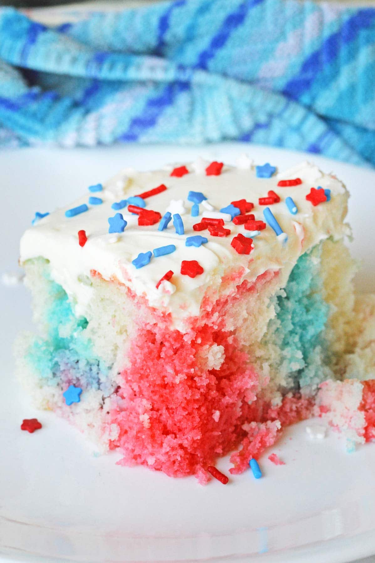 closeup of a square slice of 4th of july poke cake with white icing and red and blue sprinkles