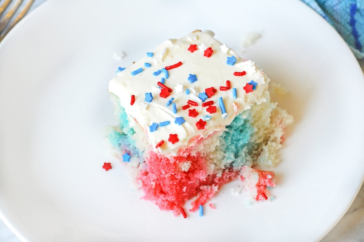 white plate with a square slice of 4th of July poke cake with red white and blue sprinkles