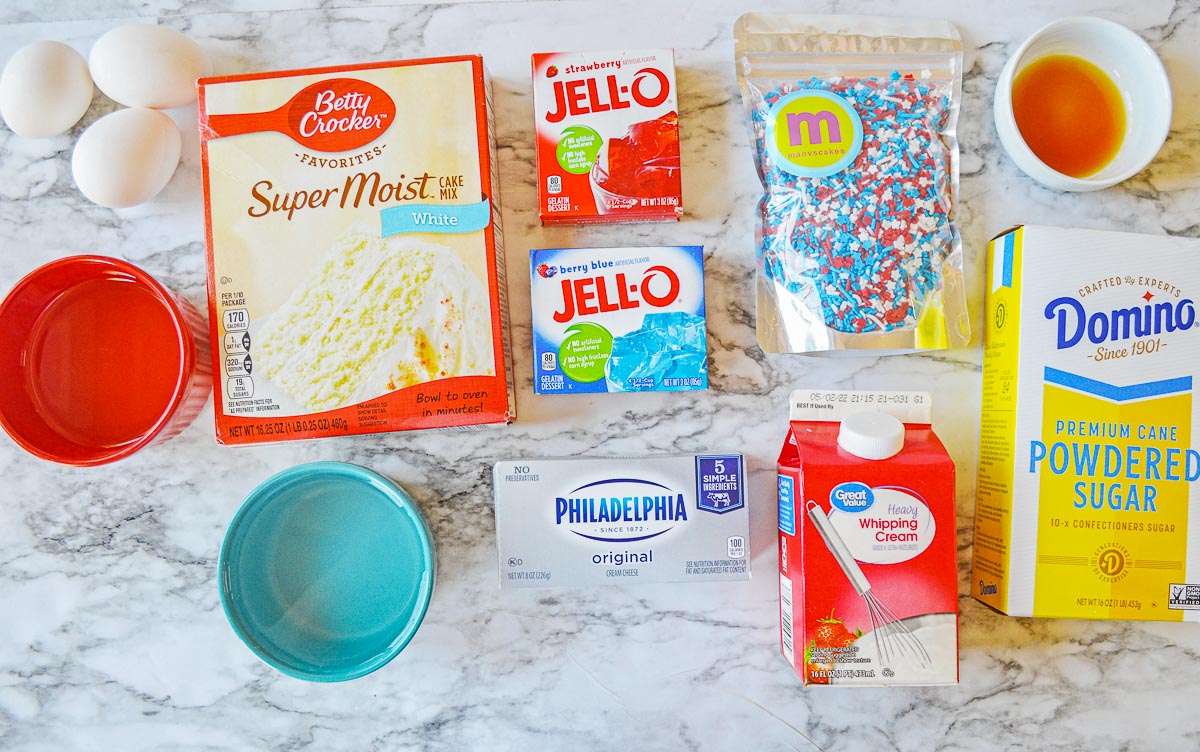incredients for red white and blue poke cake - white box cake mix, cream cheese, strawberry and berry blue jello, whipping cream, powdered sugar, eggs and vanilla