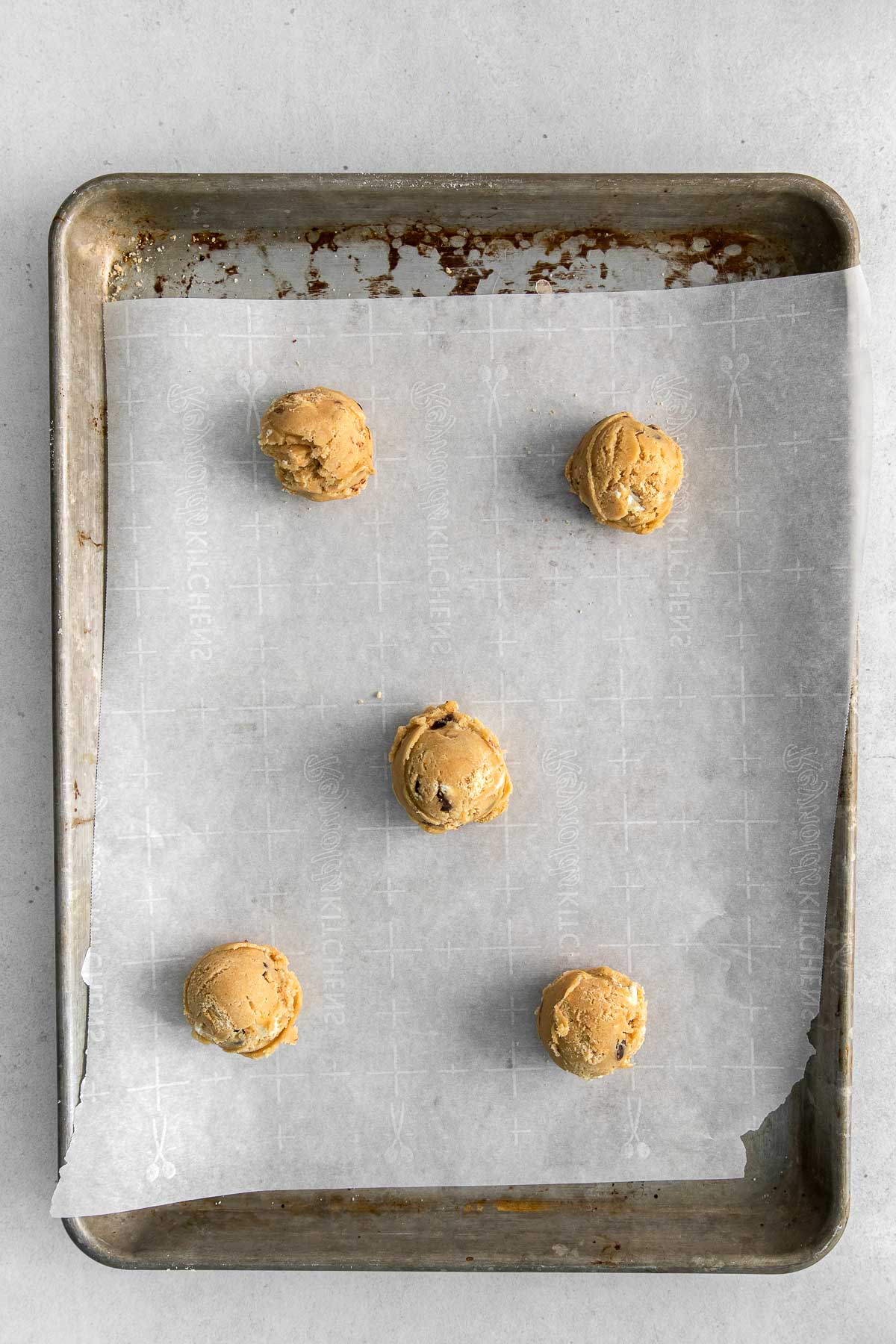 five cookie dough balls on a baking sheet lined with parchment paper