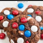 three chocolate brownie cookies with red white and blue m&m candies laying on a white plate