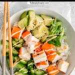 white bowl full of imitation crab, avocado and diced cucumber with spicy mayo drizzled over top