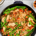 black cast iron pan with chicken stir fry with cashews, snow peas, carrots and rice noodles