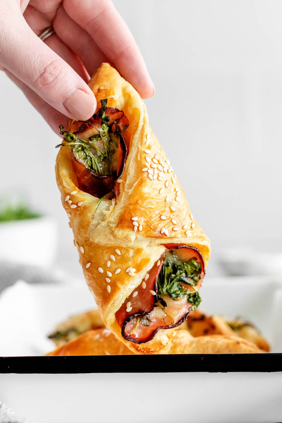 woman's fingers holding up a ham and cheese puff pastry