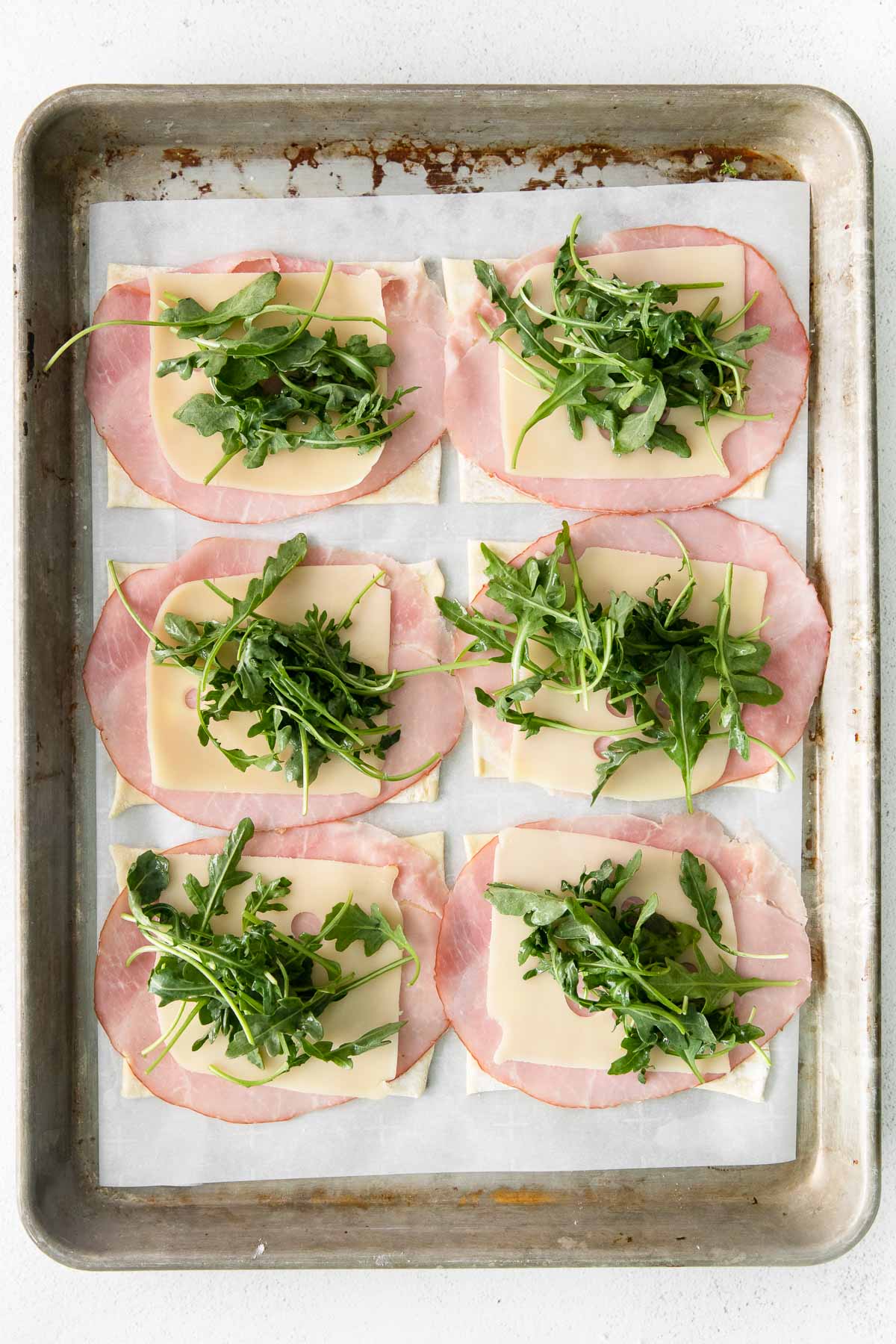 six puff pastry squares with a slice of ham and swiss cheese with arugula on top