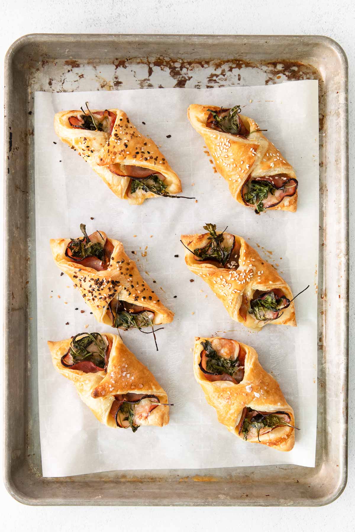 six baked puff pastries with ham and cheese inside on white parchment paper lined baking sheet