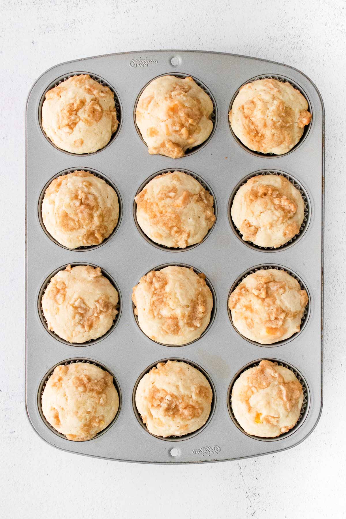 muffin tin with twelve peach muffins with crumb topping