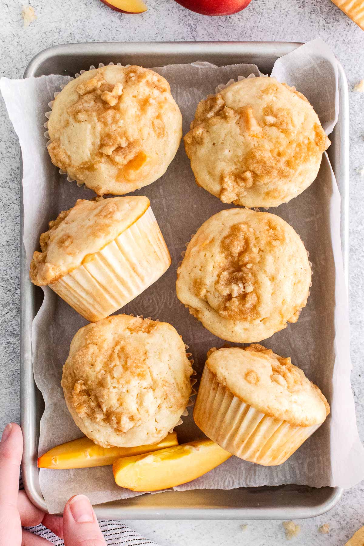 six peach muffins with crumb topping on a small silver baking sheet