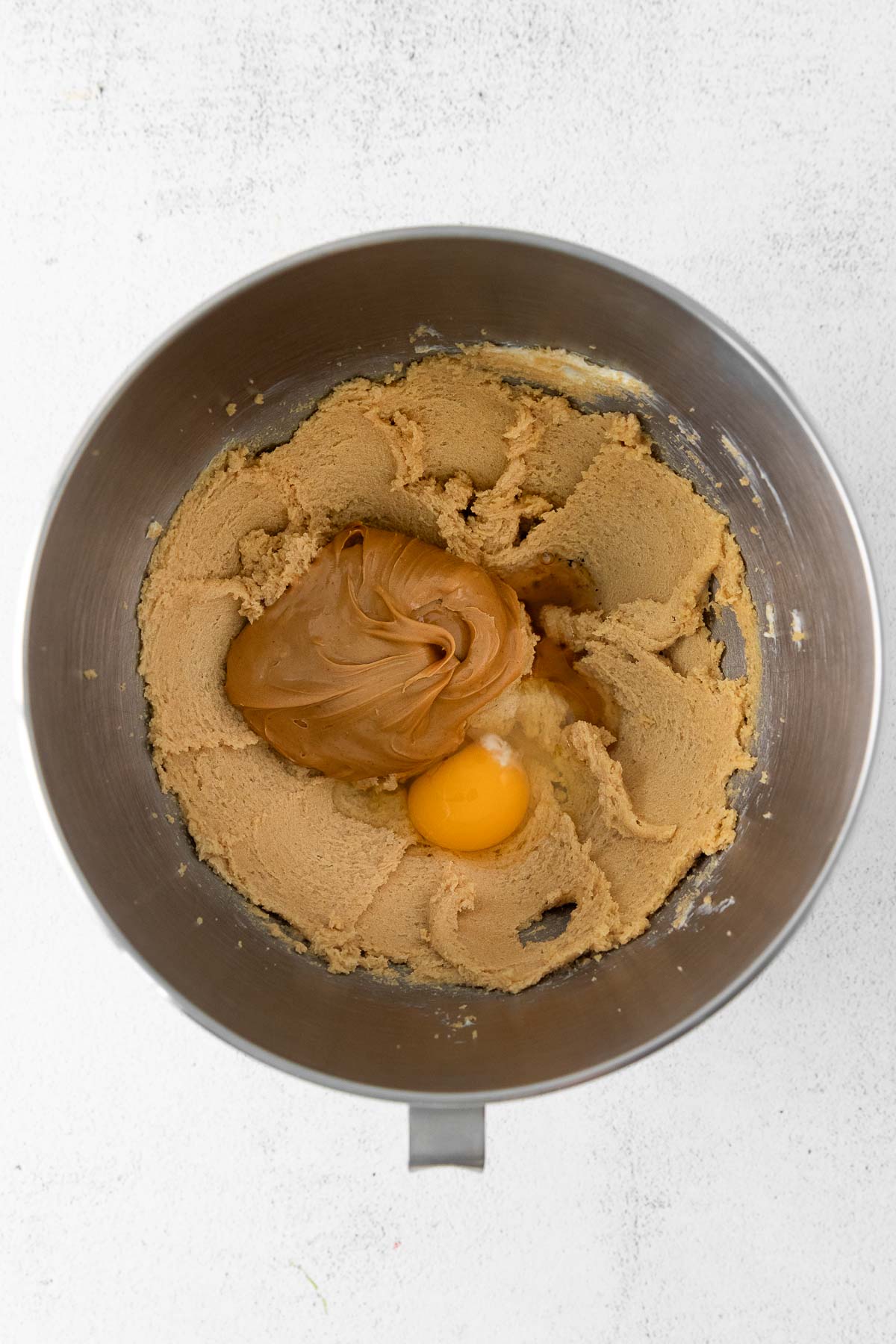 silver mixing bowl with creamed butter, creamy peanut butter and a raw egg