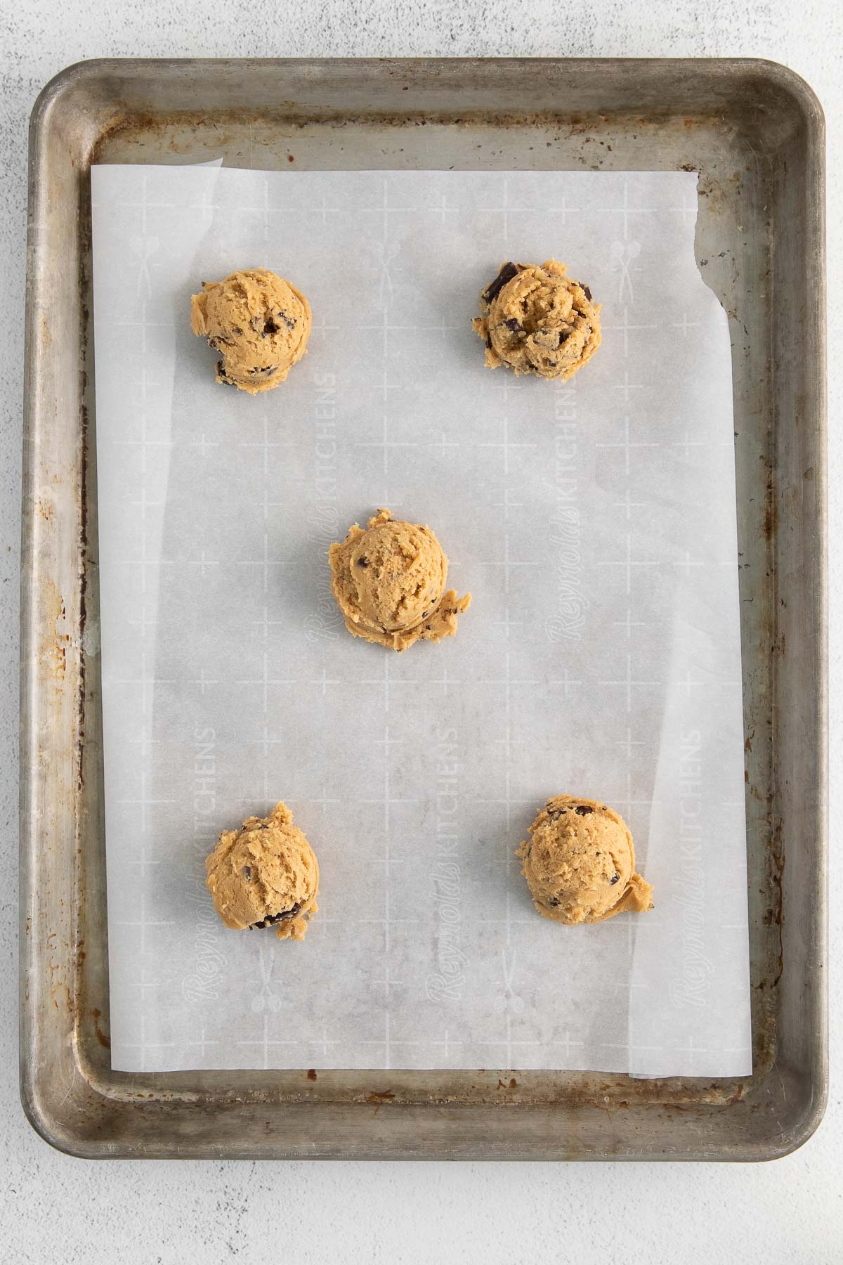 five cookie dough balls on a silver baking sheet with white parchment paper