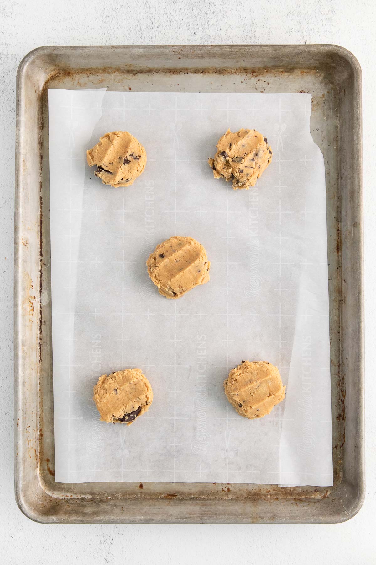 five raw peanut butter cookies with chocolate chunks added on a parchment lined baking sheet.