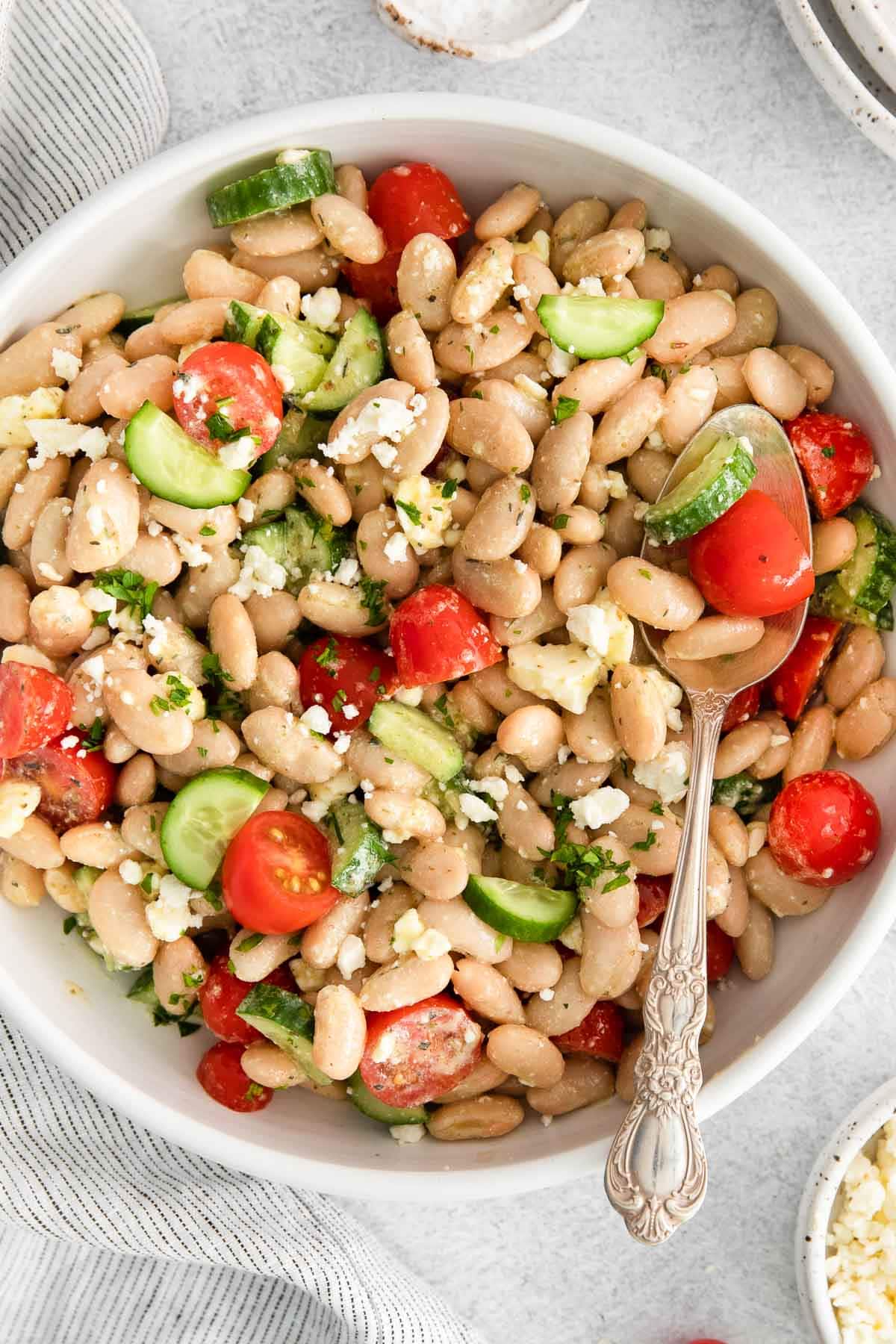 closeup of mediterranean white bean salad with cucumbers, tomatoes and feta cheese crumbles with an antique serving spoon