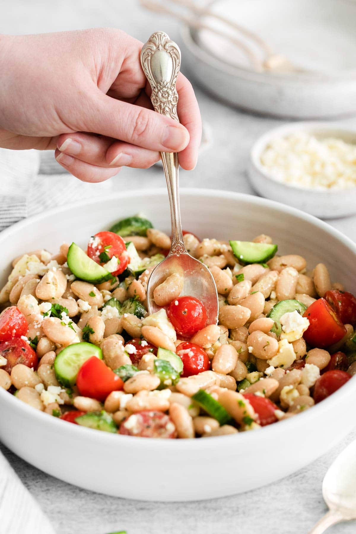 white serving bowl with white bean salad being scooped out with an antique silver spoon