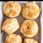 six peach muffins with crumb topping on a small baking sheet with text overlay that reads peach cobbler muffins