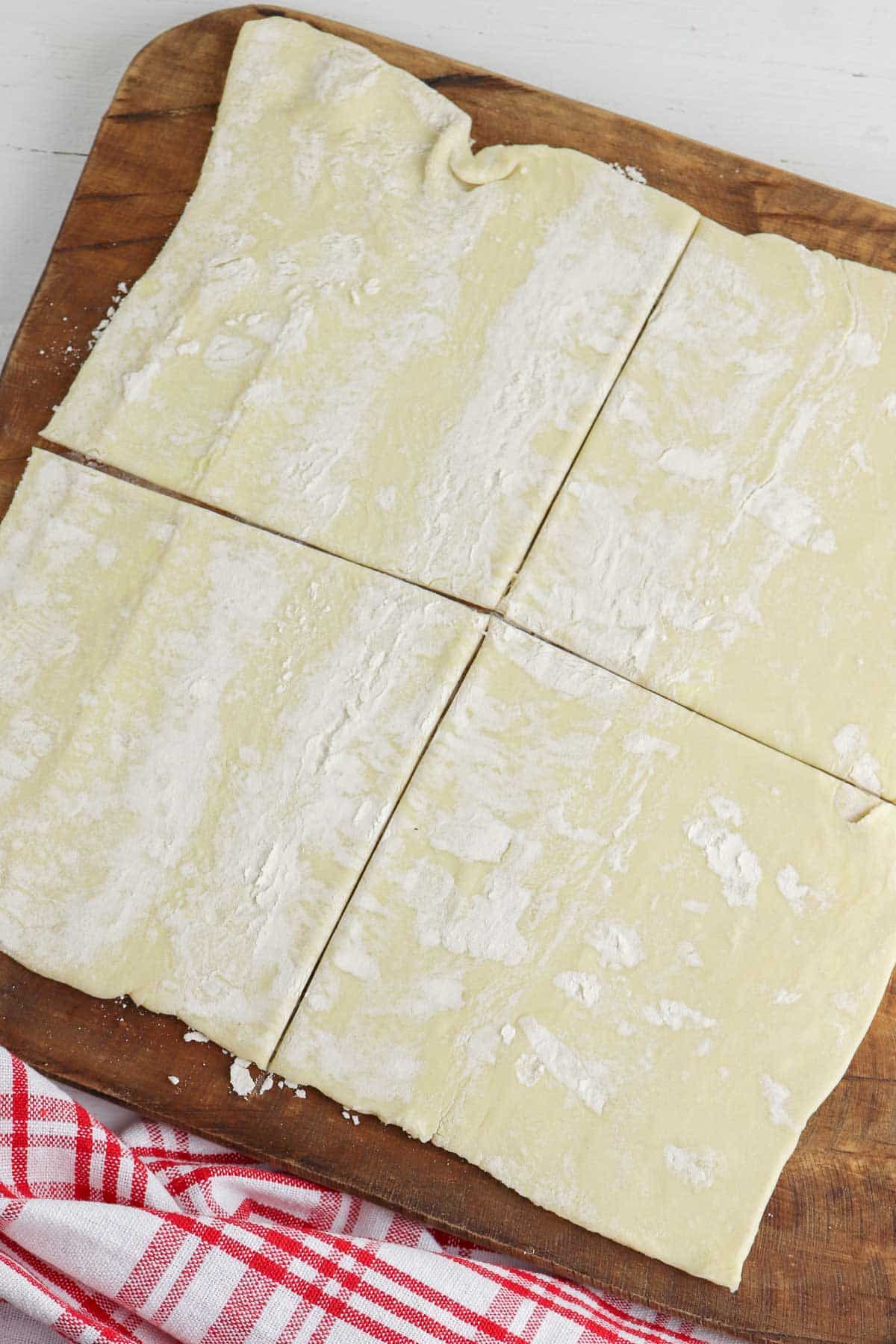 puff pastry dough cut into 4 equal squares on a wood cutting board.