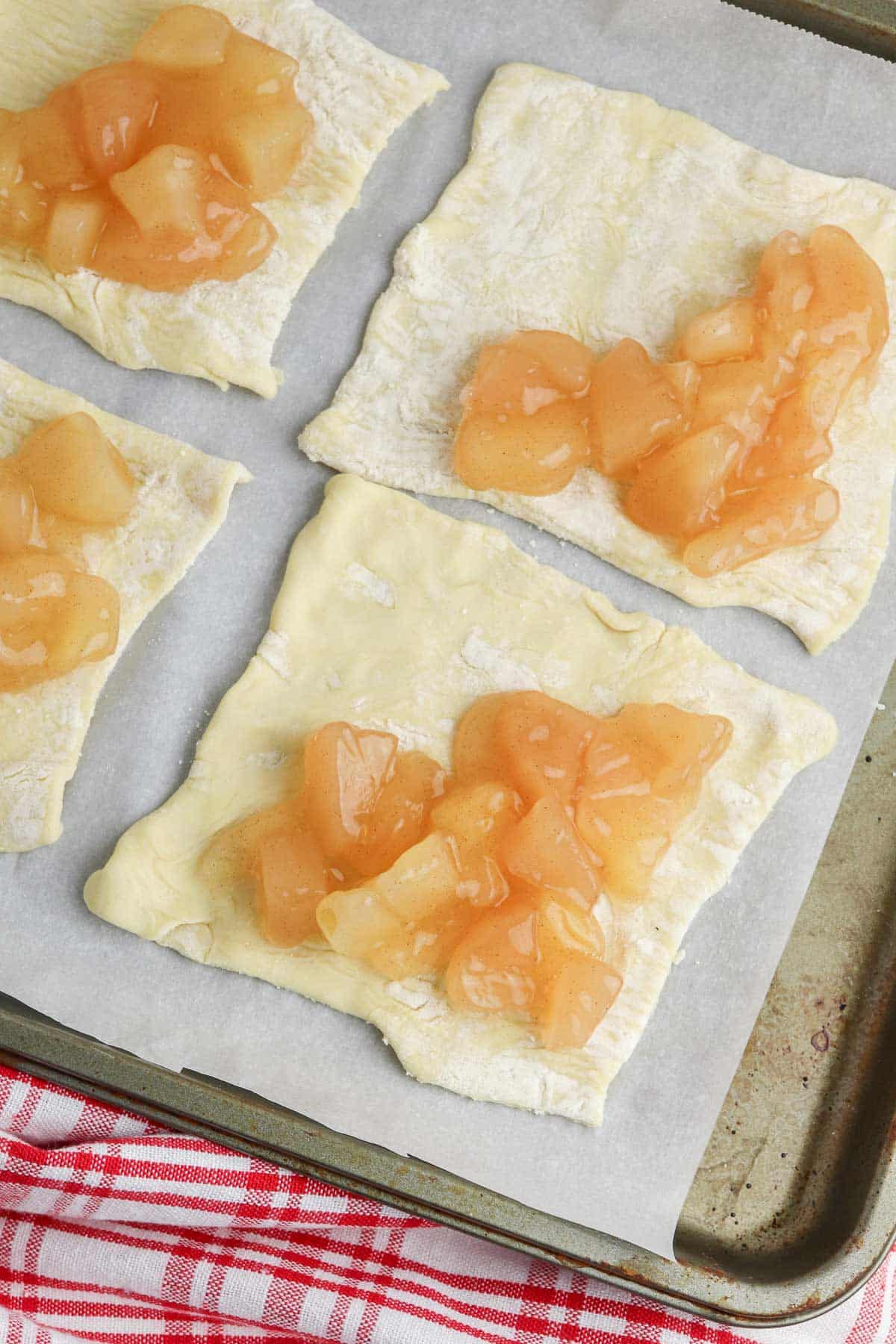 baking sheet with four puff pastry squares topped with diced apple filling.