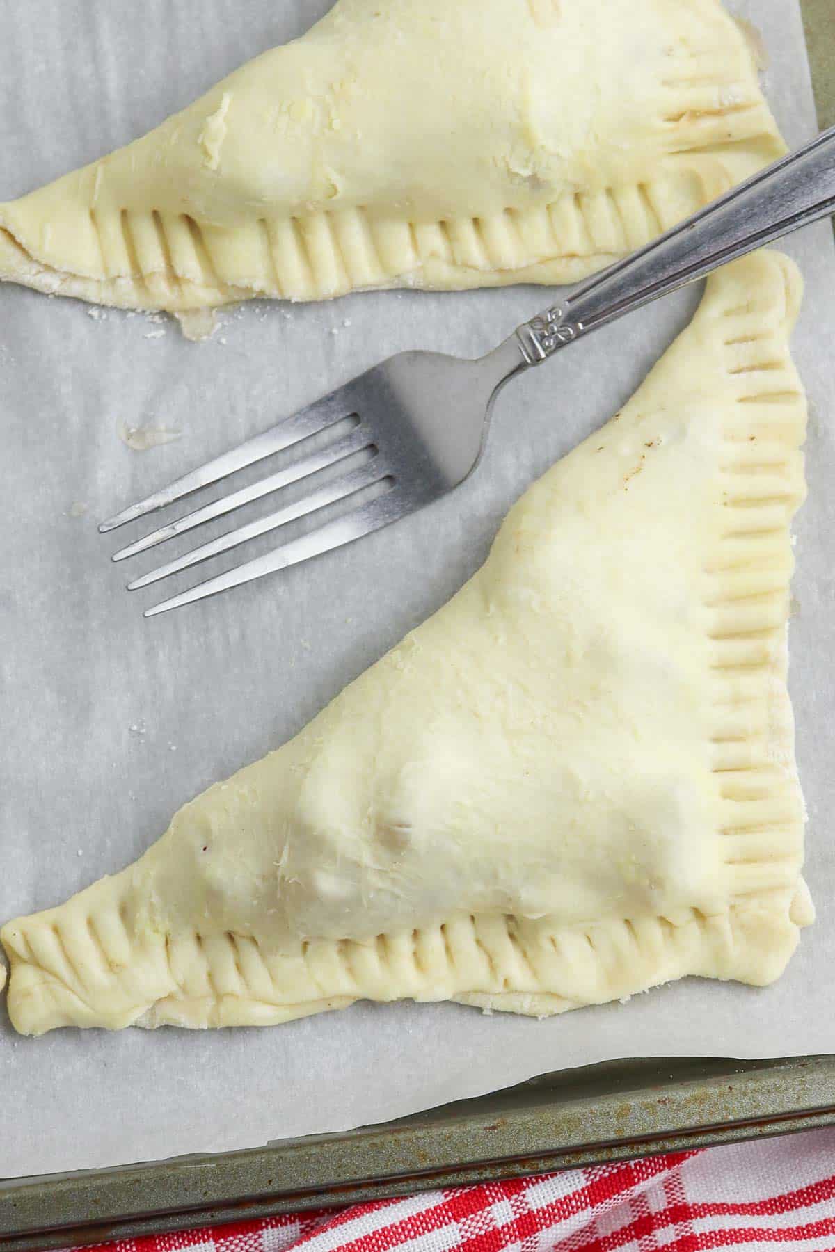 uncooked apple turnover with crimped edges on parchment paper lined baking sheet.