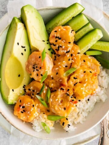 closeup of bang bang shrimp over white rice with avocado and cucumber