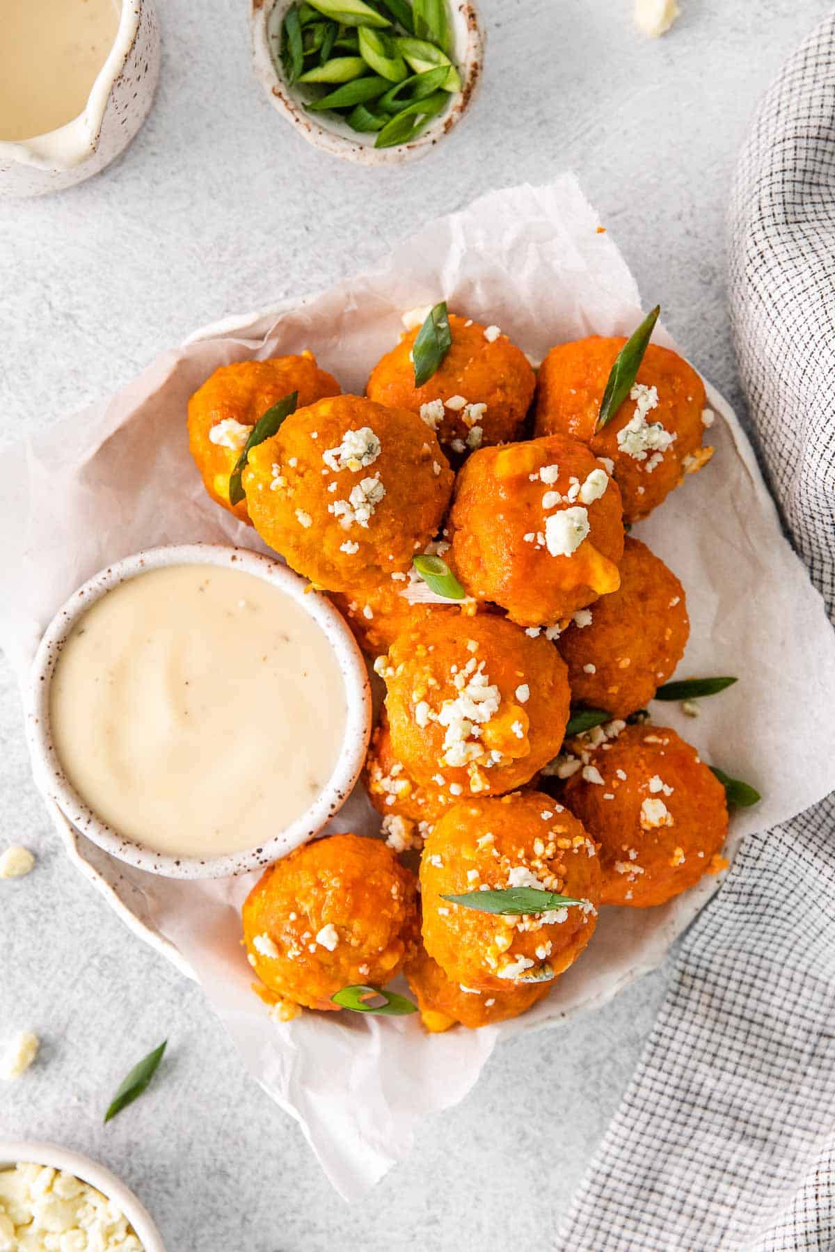 several buffalo chicken meatballs sprinkled with blue cheese crumbles on a plate with white parchment paper and a small bowl of blue cheese dressing.