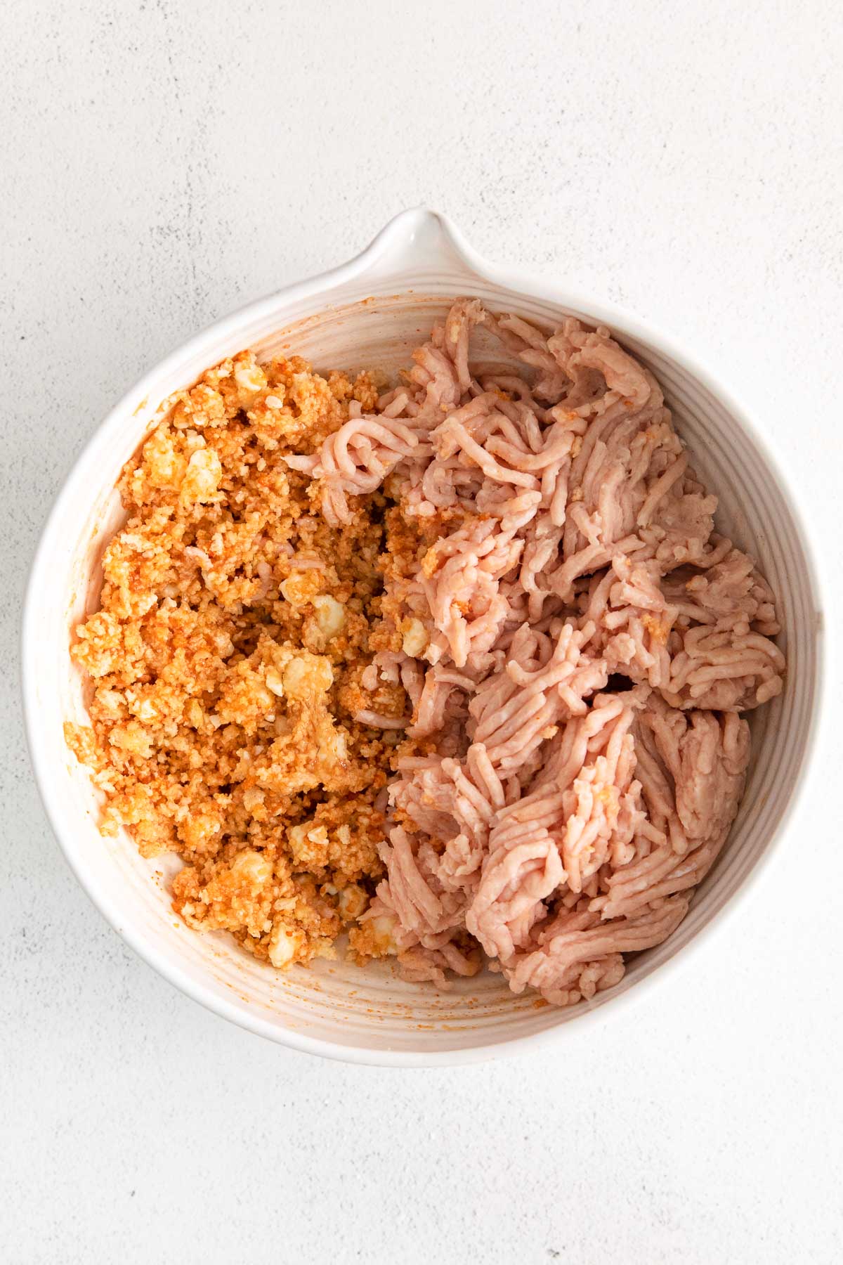 raw ground chicken with buffalo sauce mixture in a white bowl