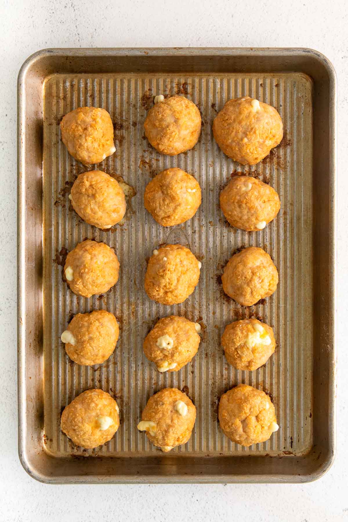 fifteen cooked buffalo chicken meatballs lined in rows on a baking sheet
