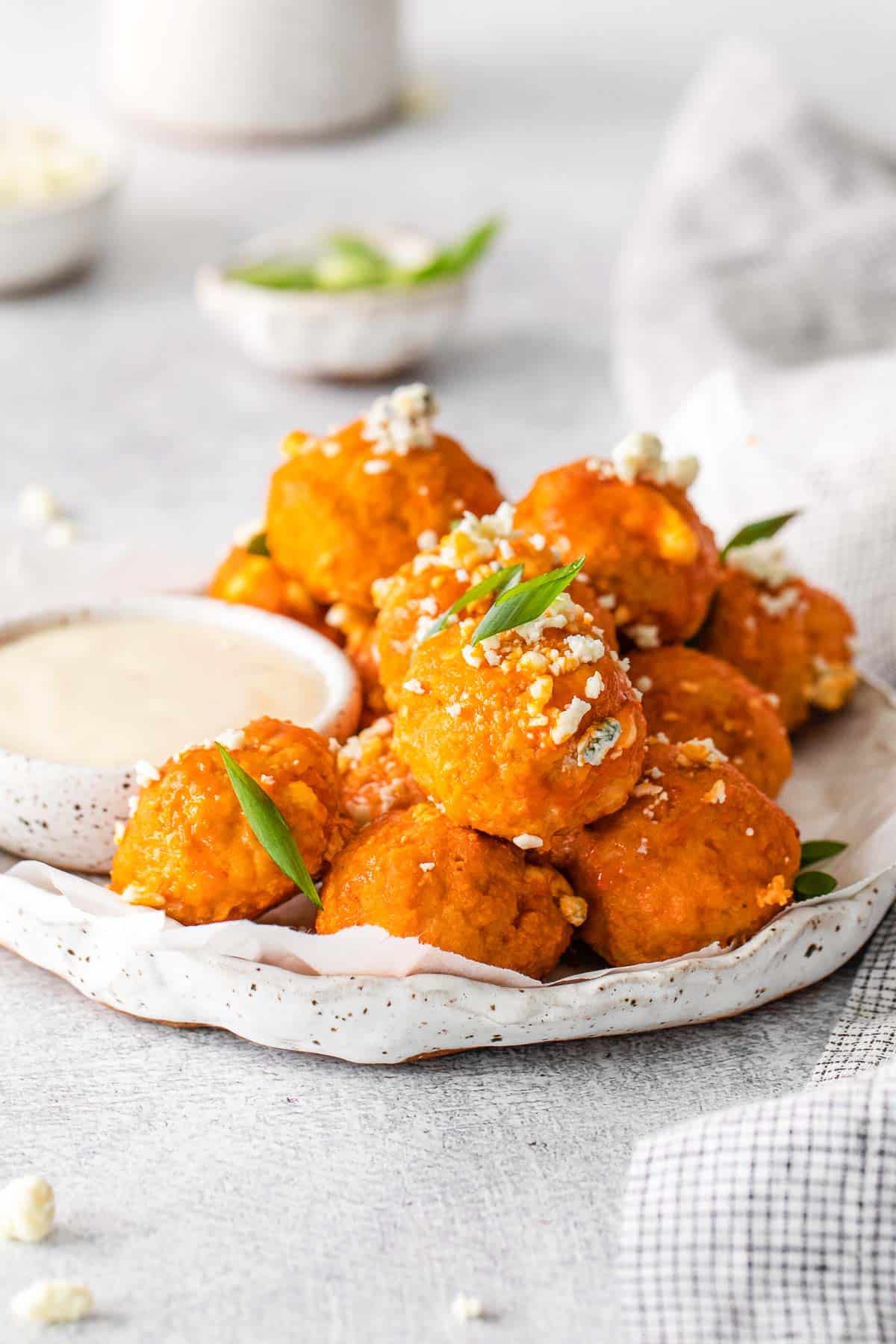 several buffalo chicken meatballs on a white plate with a small bowl of dressing on the side