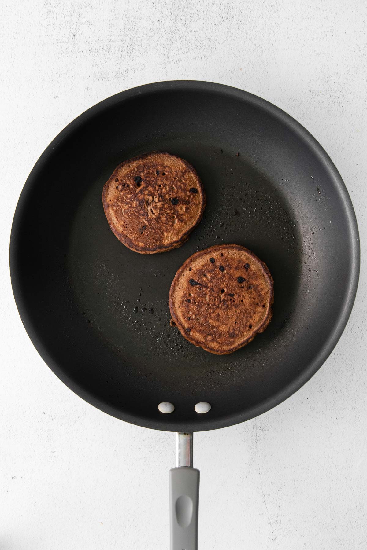 black skillet with two chocolate pancakes cooking