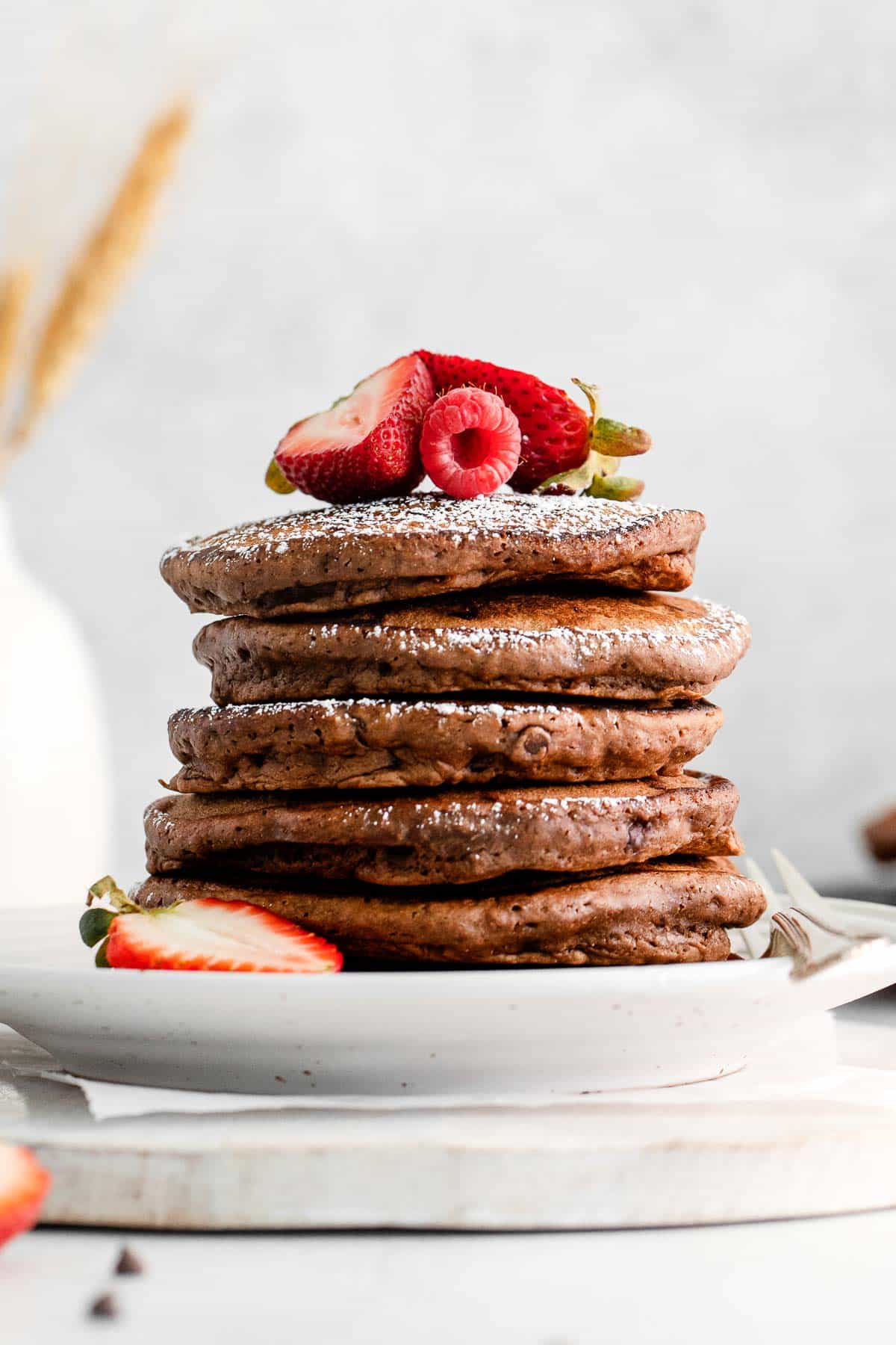 stack of five chocolate pancakes topped with powdered sugar and strawberries halves