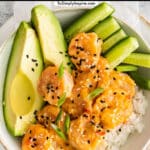 white bowl with bang bang shrimp over rice with avocado slices and cucumber slices.