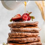 stack of five chocolate pancakes topped with fresh berries with syrup being poured over top