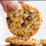 woman's fingers holding a oatmeal cookie over a stack of three cookies