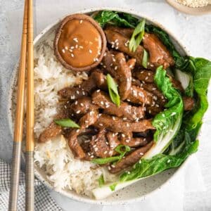 closeup of a korean beef bolgogi bowl with white rice, steak strips and boy choy.