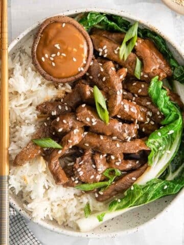 closeup of a korean beef bolgogi bowl with white rice, steak strips and boy choy.