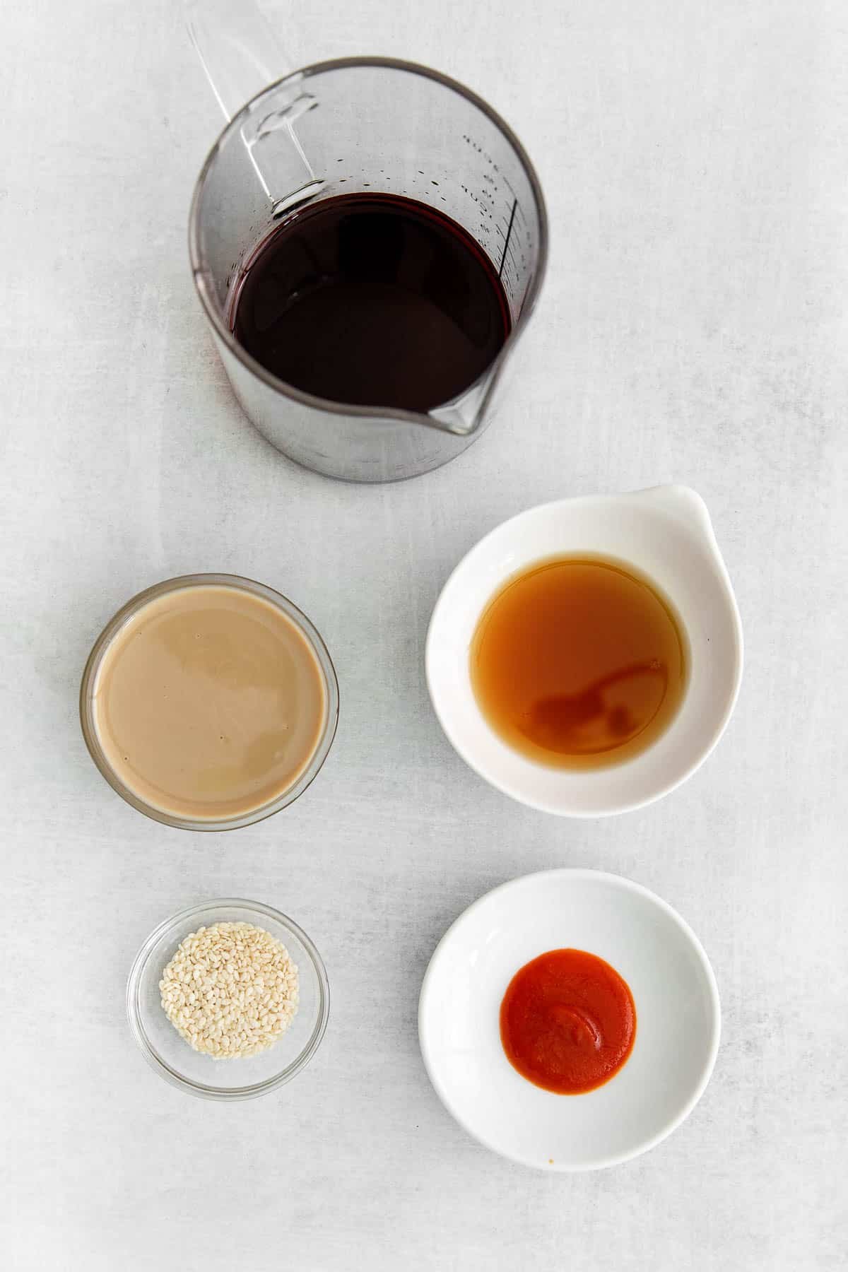 several glass bowls with ingredients for a tahini soy sauce - tahini, soy sauce, sriracha, sesame oil and sesame seeds