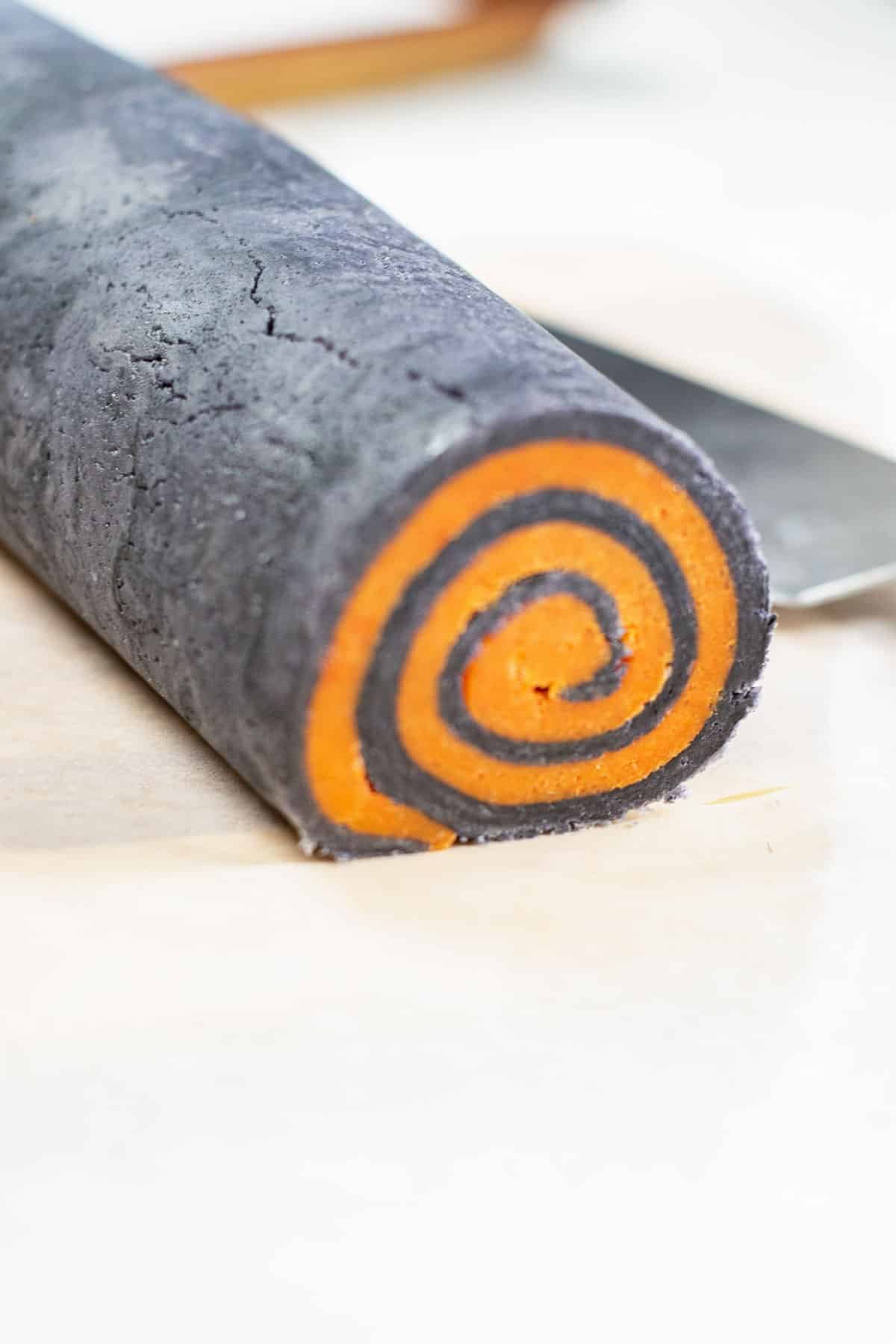 a roll of black sugar cookie dough with orange dough rolled inside of it for halloween pinwheel cookies