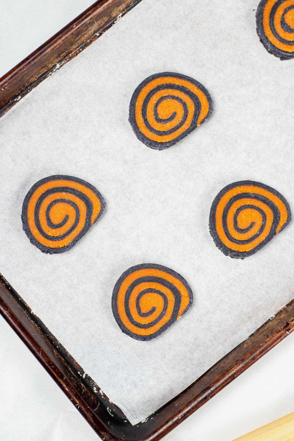 five uncooked slices of black and orange pinwheel cookies in a cookie sheet lined with parchment paper.