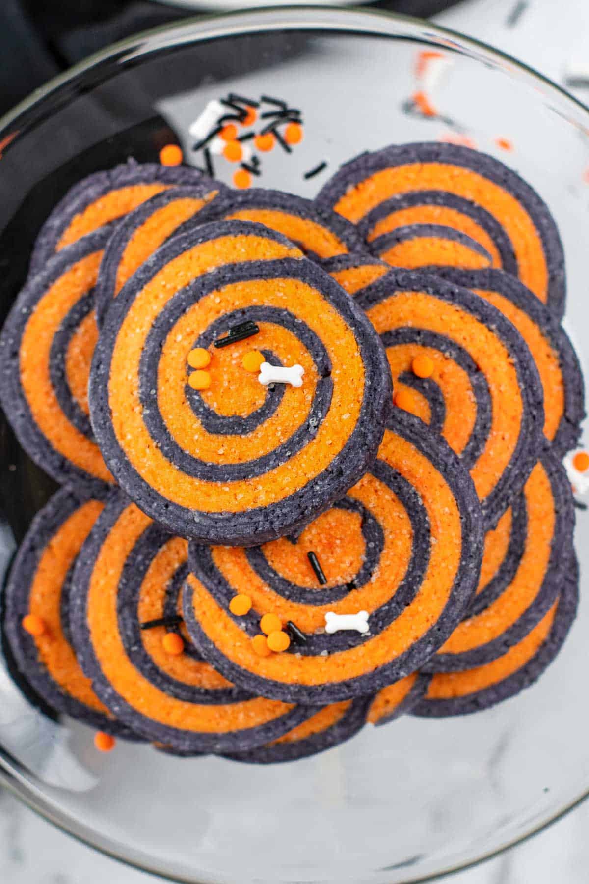 a stack of orange and black halloween sugar cookies on a glass plate.