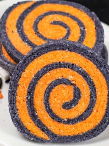 closeup of a black and orange halloween pinwheel cookie on a white plate.