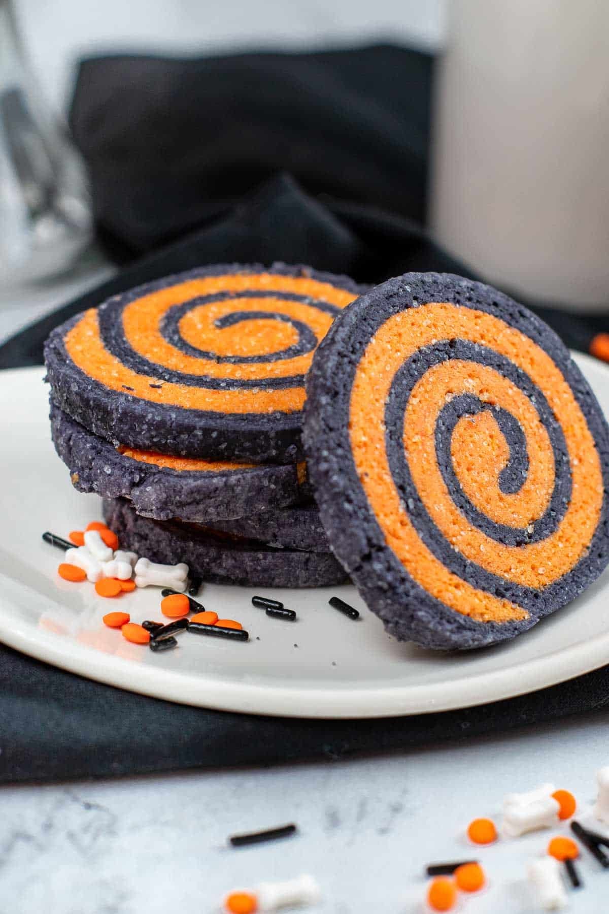 five black and orange halloween pinwheel cookies stacked on a white plate.