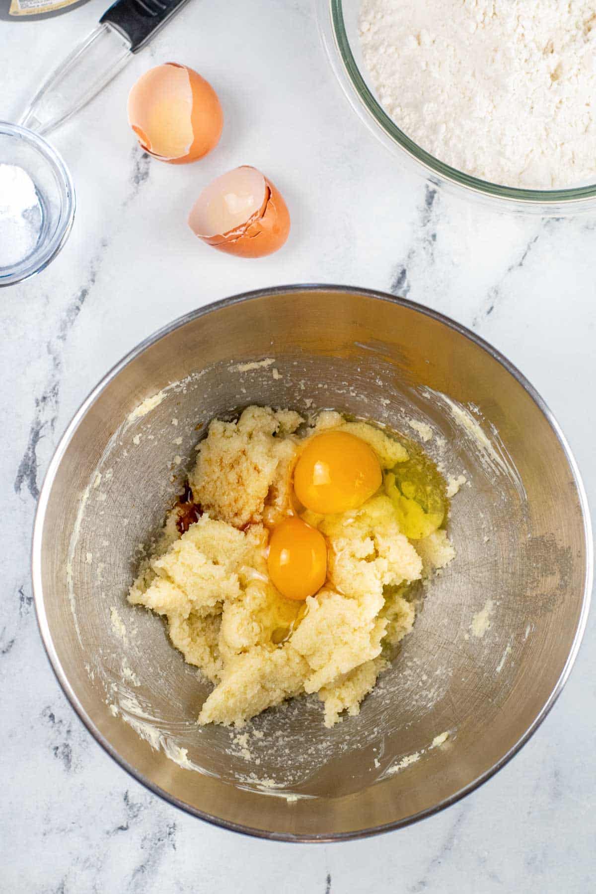 silver mixing bowl with with two eggs broken over creamed butter