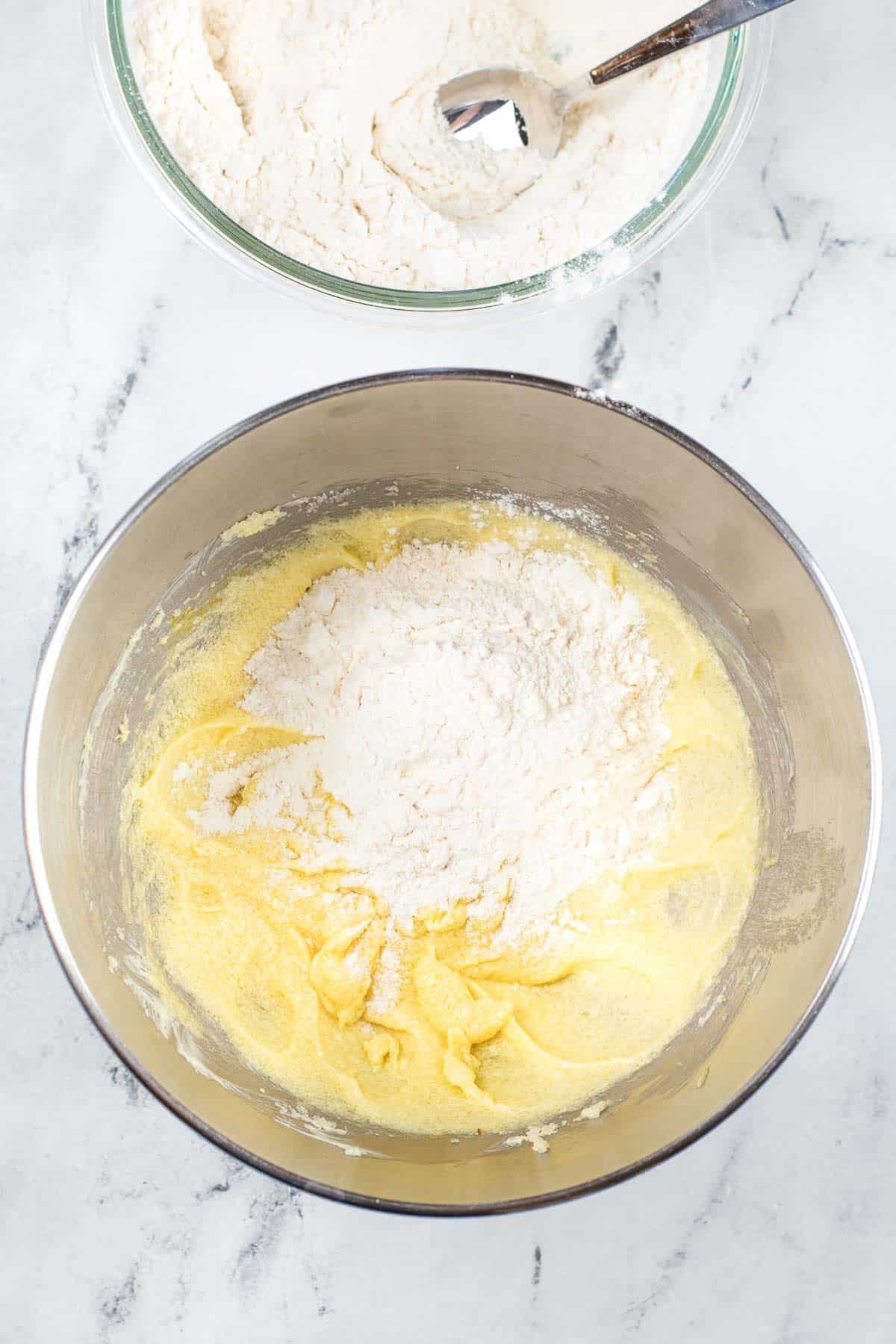 silver mixing bowl with flour being added to creamed butter, eggs and sugar