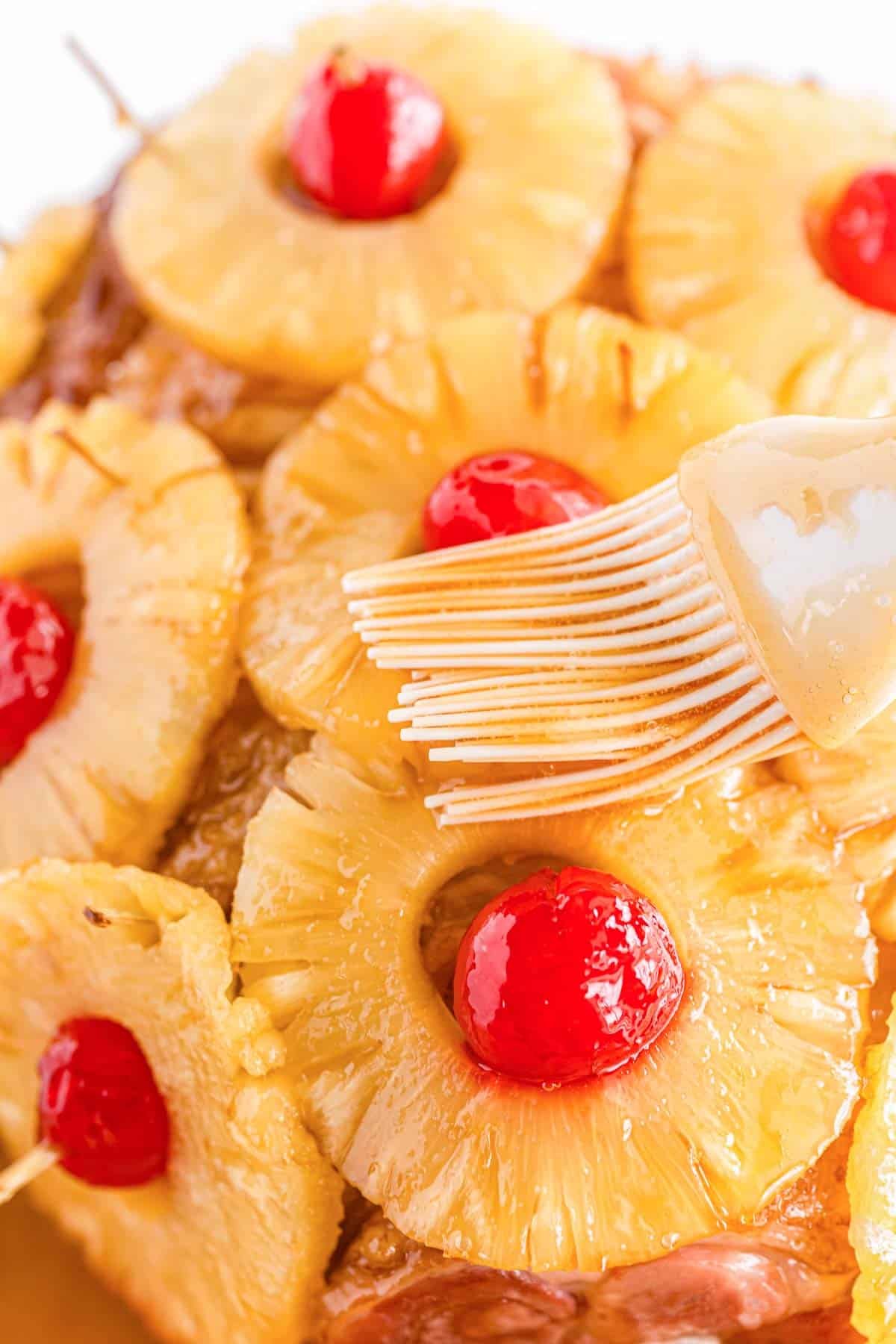 closeup of pineapple rings with cherries in the centers being brushed with honey glaze.