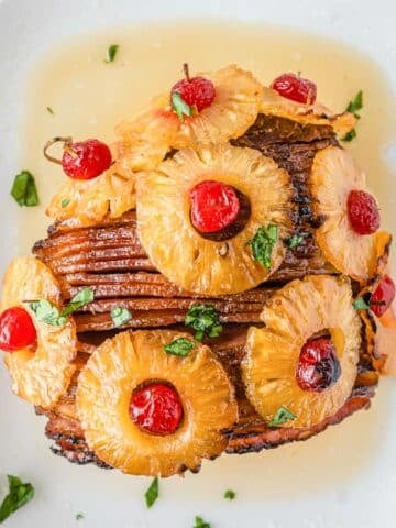 closeup of sliced honey baked ham topped with pineapple with cherries in the centers.