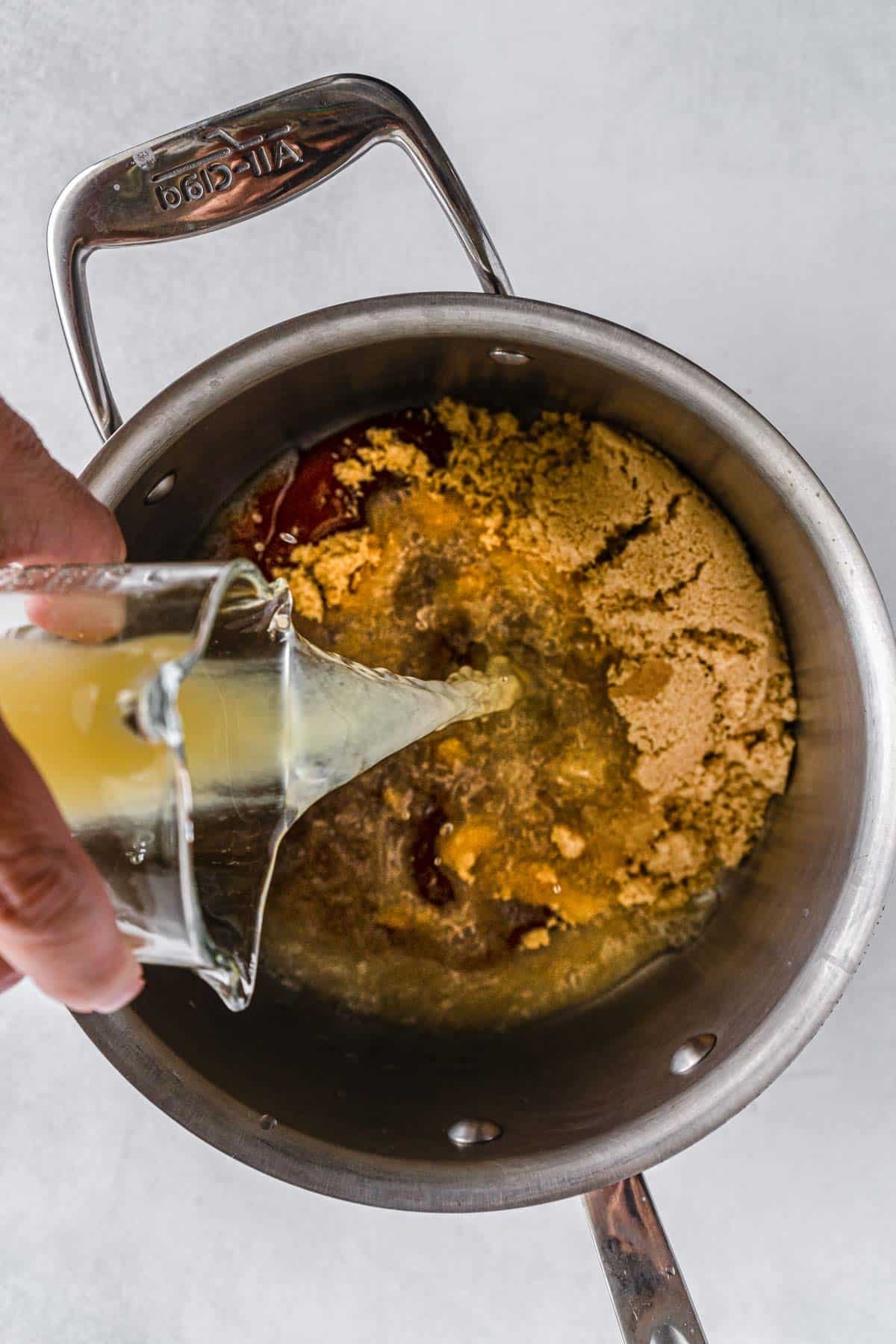 juice being poured into a stainless steel pot with brown sugar mixture.
