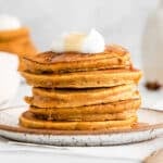 closeup of a stack of five pumpkin pancakes with a dollop of whipped cream and drizzled with syrup