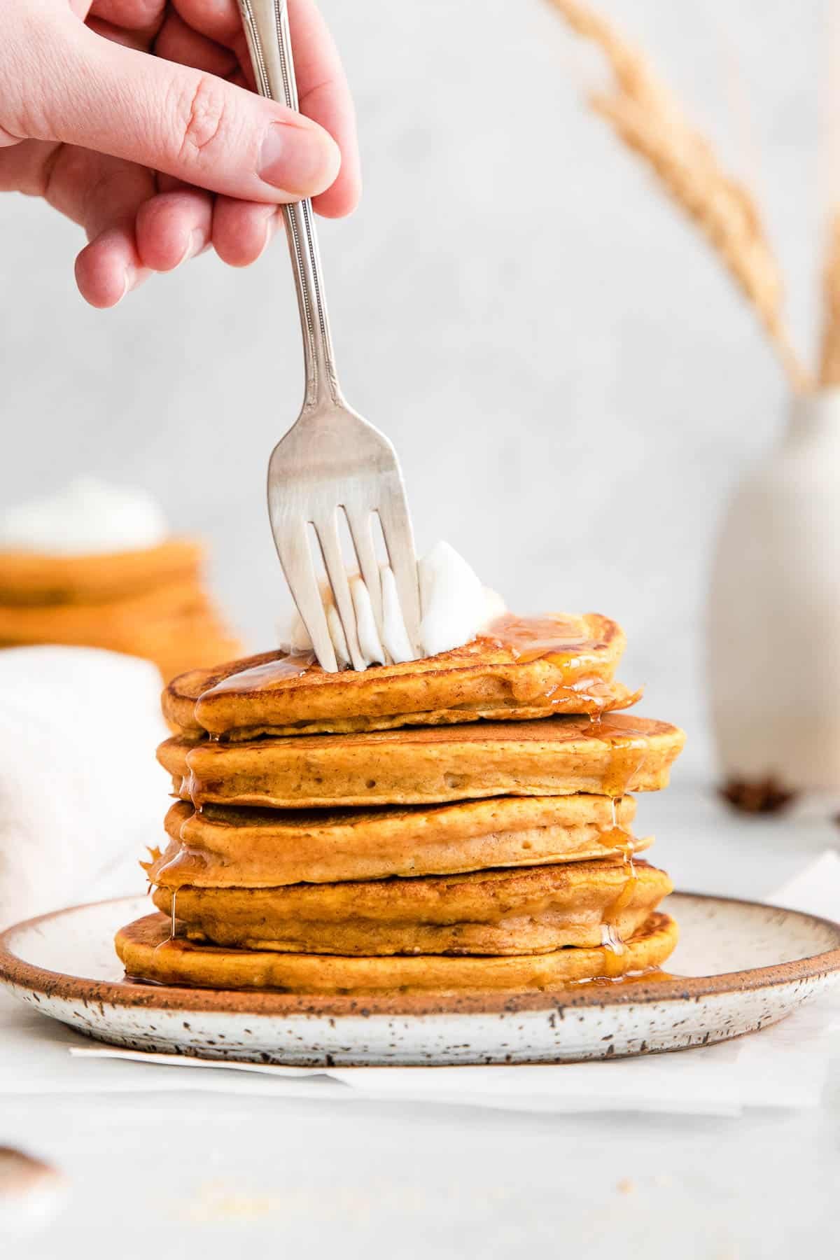 stack of five pumpkin pancakes drizzled maple syrup with a fork sticking in the top