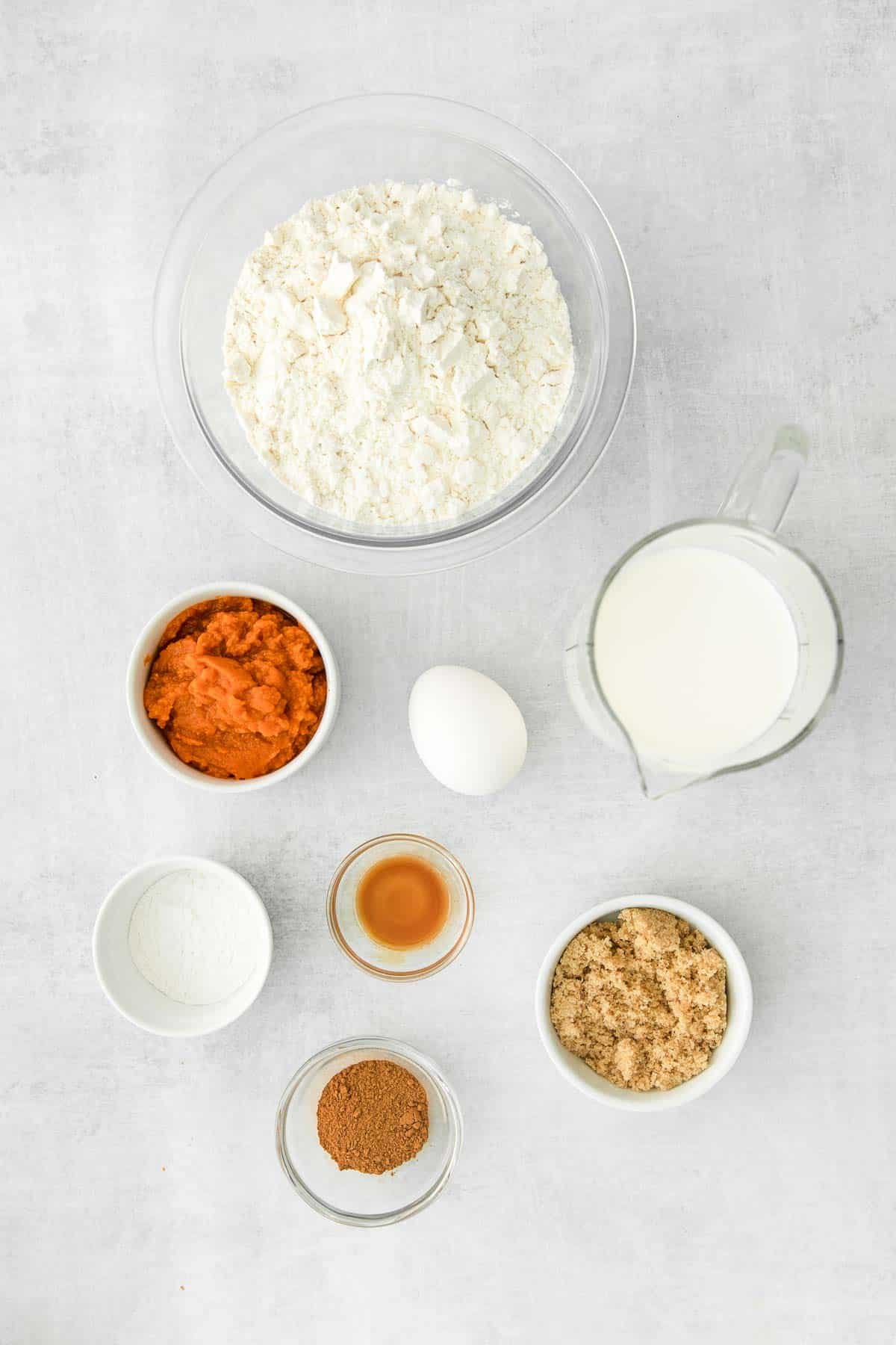 several small glass bowls with ingredients for pumpkin pancakes - flour, pumpkin puree, brown sugar, cinnamon, egg, milk, baking soda