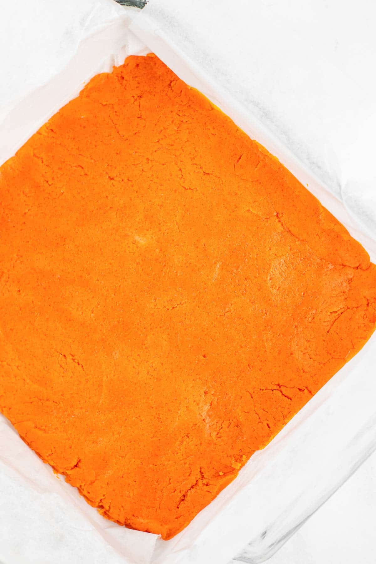 orange cookie dough pressed into a square glass baking dish.