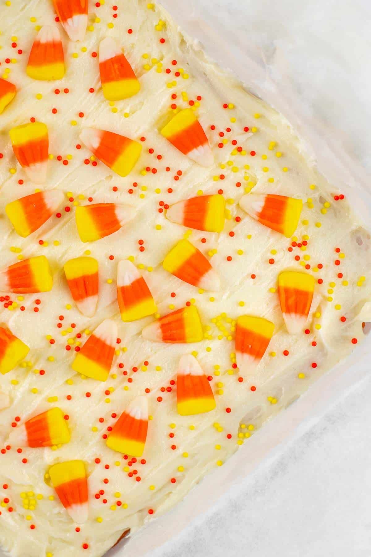 candy corn and orange and yellow sprinkles on white frosting in a square baking dish.