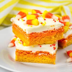 stack of two orange and yellow layered sugar cookie bars with white frosting and topped with candy corn and sprinkles.